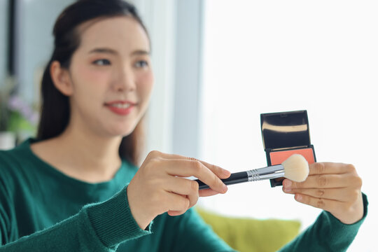 Asian woman filming beauty vlog tutorial with ring light, reviewing cosmetics and makeup concept.