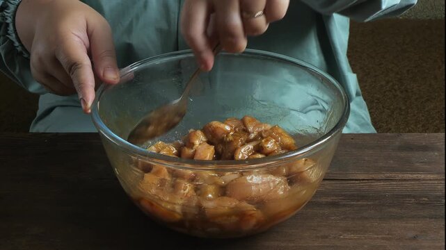 A woman's hands marinate chicken fillet in teriyaki sauce with spices and garlic in a glass bowl. Close-up.