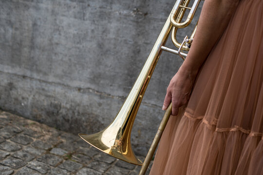 Detail close-up shot of a woman holding a golden trombone slide and bell wearing an elegant tulle skirt outdoors