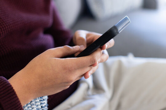 Adult African American male holding and scrolling black smartphone on couch with maroon sweater