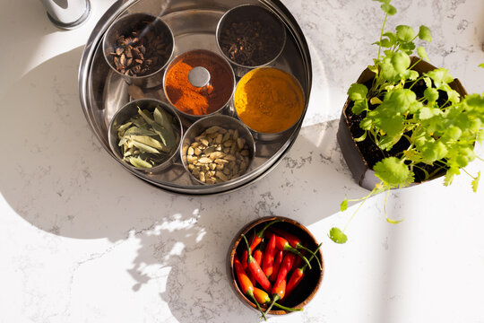 Stainless steel spice tin sitting on marble counter by window catching light, cilantro red chilis