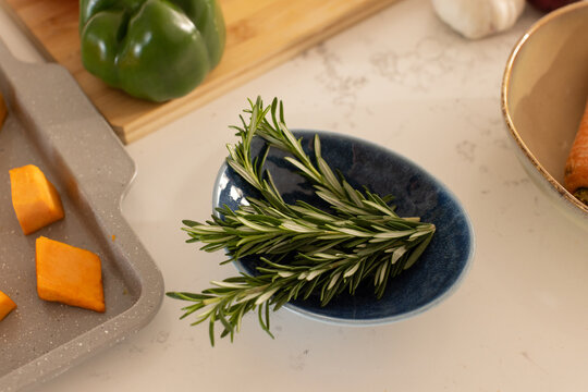 Fresh rosemary sprig is resting in small blue dish on marble countertop, with cubed orange squash