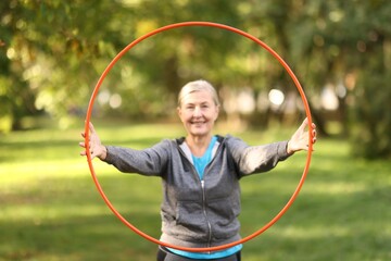 Senior woman exercising with hula hoop outdoors, selective focus © New Africa