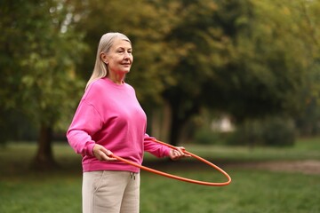 Senior woman exercising with hula hoop outdoors. Space for text © New Africa