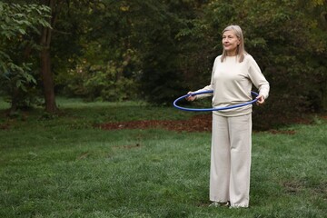 Senior woman exercising with hula hoop outdoors, space for text © New Africa