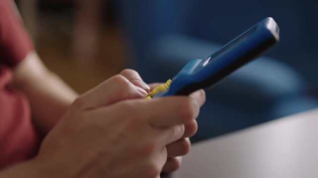 Closeup of male hands holding and playing old school handheld video game, pressing yellow buttons of blue device for leisure and nostalgic entertainment at home. Shooting in slow motion.