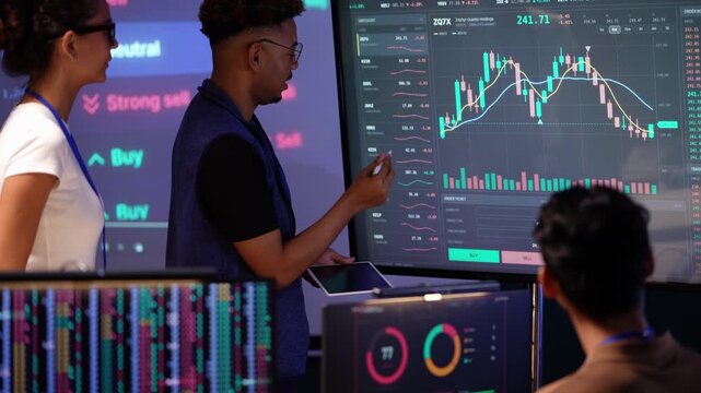 Black analyst in a blue vest gestures at an upward candlestick pattern, then writes on a tablet and speaks while a Latina colleague listens and an Asian man looks on
