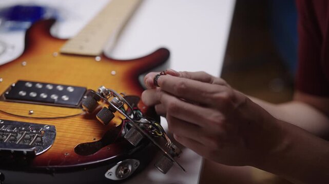 Luthier assembling electronic components of sunburst bass guitar, meticulous hands repairing potentiometer in specialized workshop for musical instruments, close-up, cropped shot, slow motion.