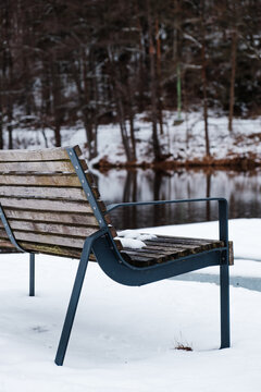 Empty wooden bench covered with snow beside a winter pond