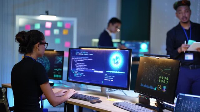 Latina developer points at the AI logo on her monitor, types code and adjusts her glasses as a Black teammate takes notes on a tablet and an Asian colleague works at the back screens
