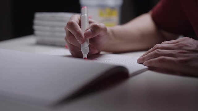 Close-up of hand using red marker to draw, color in sketchbook. Shallow depth of field focuses on creative process. Mood calm, studious and focused, closeup, cropped shot, slow motion.