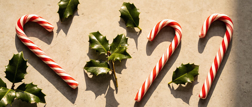 Red and white striped candy canes form the number 222 with green holly leaves on a textured beige surface