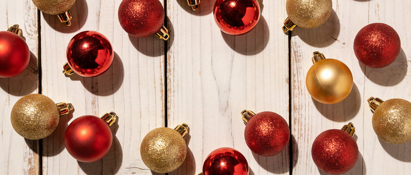 Red and gold Christmas ornaments arranged in a heart shape on a white wooden background.