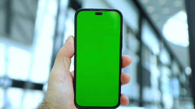 Hand holds phone with green screen. Background blurred, modern indoor space. Three keyframes, consistent scene. Phone orientation upright, fingers grip edges