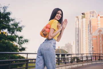 Rear photo of charming positive girl hold fruits net arm palm waving hi look camera pastime outside © deagreez