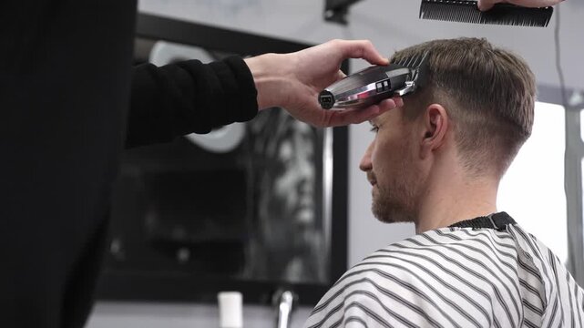 Professional barber trimming male client's hair using electric razor, creating precise haircut in contemporary barbershop setting with sleek styling tools