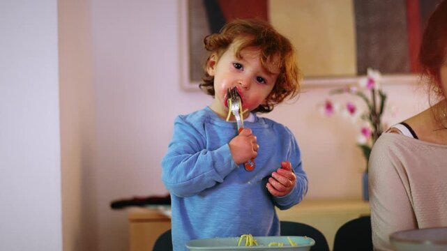Caucasian toddler eating spaghetti with a fork at the dinner table