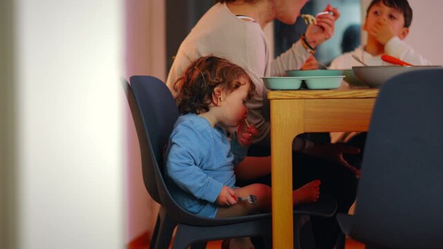 Tired Caucasian toddler playing with a fork at the family table