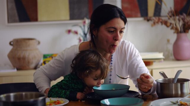 Caucasian mother eating soup with toddler sitting on her lap