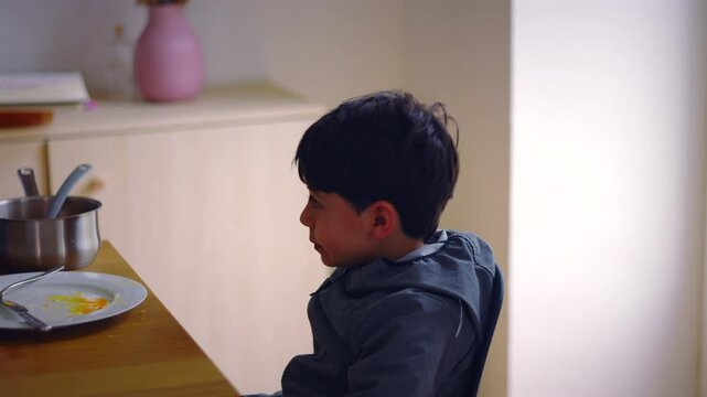 Thoughtful Caucasian boy eating a snack at the table after lunch