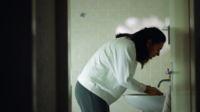 Caucasian woman washing her face at the bathroom sink