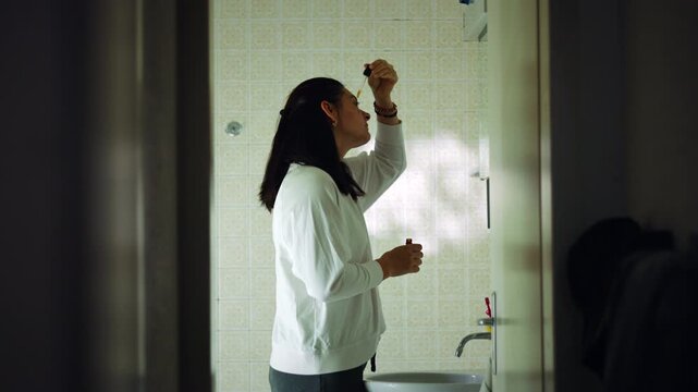 Caucasian woman applying facial serum with a dropper in the bathroom