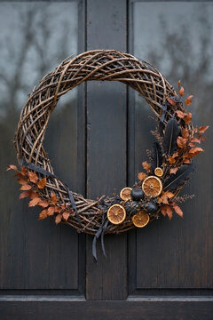 Natural wicker Halloween wreath of twisted willow branches with black feathers, dried orange slices, dark gourds and autumn foliage
