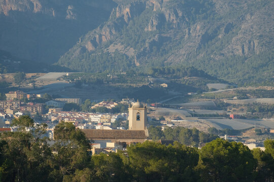 Distant view of La Nucia, Spain, with a church bell tower, town buildings, cultivated hillsides and rugged mountains in the background