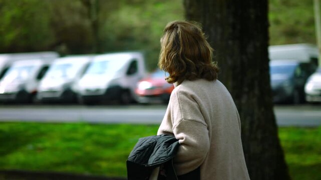 Elderly Caucasian woman walking away along a park path