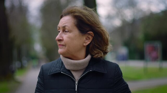 Serious Caucasian senior woman walking in the park and looking around