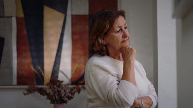 Pensive Caucasian older woman with hand on chin by the window