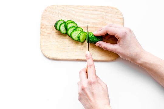 Hands cut cucumbers for salad. White background top view