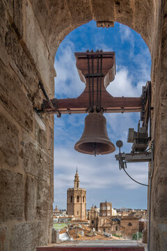 Ancient bronze bell hanging instone window of El Micalet tower, panoramic view over the historic old town roofs and the baroque bell tower of Santa Catalina church in Valencia, Spain, 