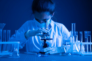 Scientist in blue-toned laboratory adjusts microscope objective turret during pharmaceutical drug discovery research © Mihail