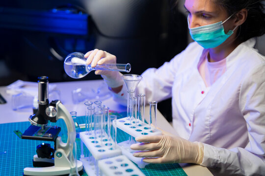 Female Scientist Pouring Vaccine Solution From Flask Into Test Tubes For Medical Research