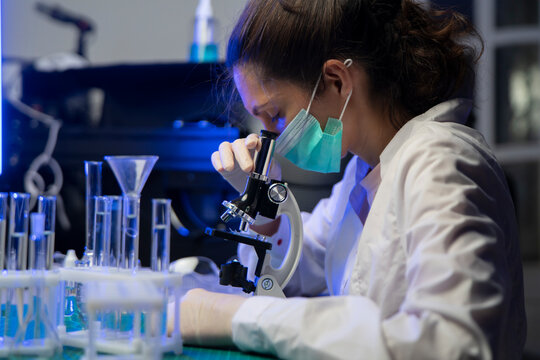 Female Researcher Examining Vaccine Sample Under Microscope In Medical Research Laboratory
