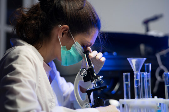 Concentrated female laboratory worker examining chemical cell structure through optical microscope lens.