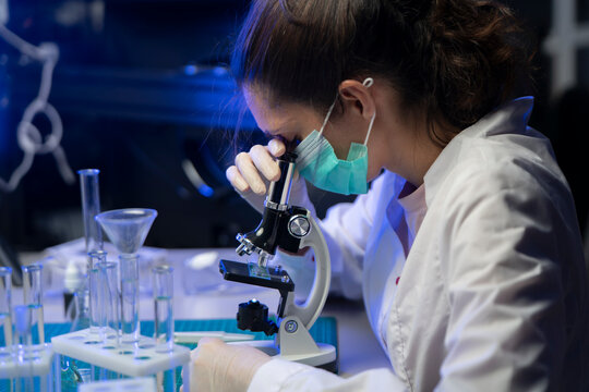Female lab technician conducting precise microscopic analysis of virus sample in modern biotechnology room.