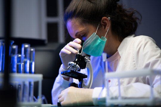 Dedicated female chemist carefully investigating liquid biology samples using advanced lab microscope.