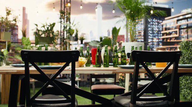 Close-up of beer bottles, orange juice and plates on a rooftop barbecue table shows refreshments and snacks arranged for casual outdoor entertainment and a city terrace party with friends.