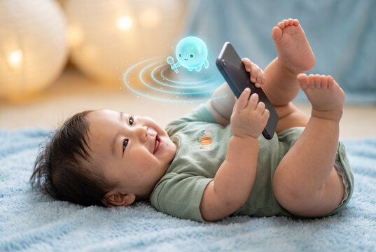 Asian baby lying on fluffy blue rug holding smartphone and looking at glowing AI chatbot hologram with microphone and sound waves, showcasing concept of artificial intelligence for infants, voice assi