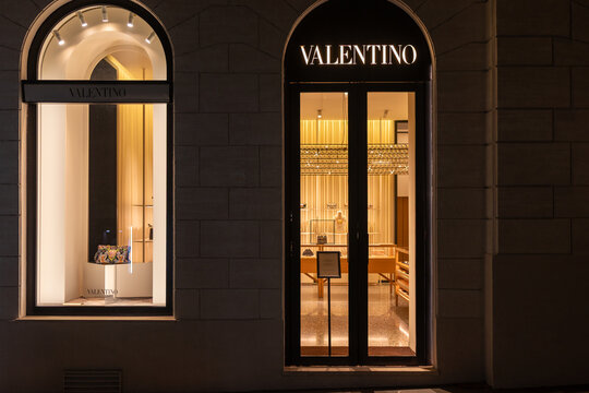 Valentino boutique facade with illuminated sign and lit window display at night in Rome, Italy