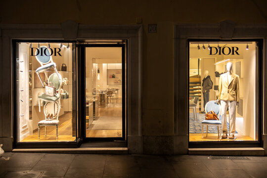 Dior boutique storefront windows illuminated at night with mannequins and chairs on a street in Rome, Italy