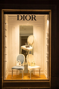 Dior boutique window display with handbags and high heel sandals on elegant chairs at night in Rome