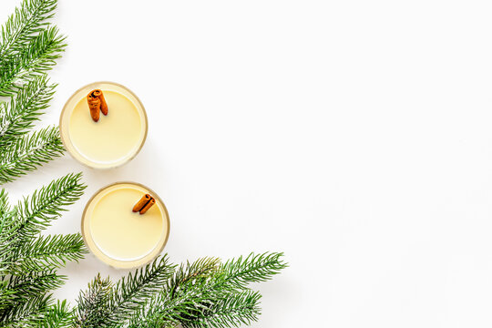 Winter attributes. Glasses of classic eggnog with spices near spruce branch on white background top view copyspace