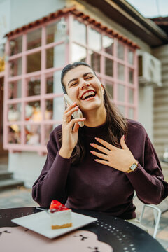 Happy woman laughing during a phone conversation at a cafe with cake