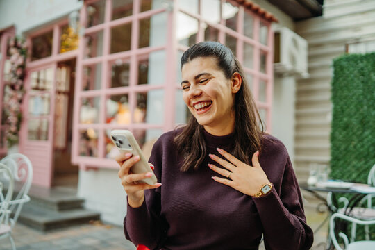 Woman laughing while reading a smartphone at an outdoor cafe
