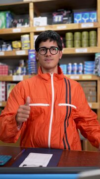Friendly store clerk standing behind counter, smiling and showing thumbs up gesture