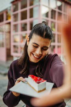Woman smiling with strawberry cheesecake in a colorful cafe