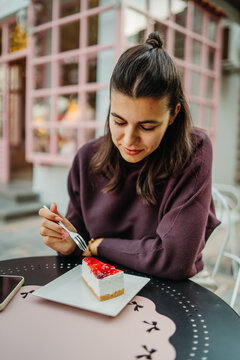 Woman enjoying strawberry cheesecake at an outdoor cafe